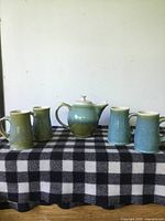 Full set of one teapot and four mugs placed on a black and white checkered cloth.