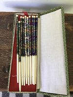Top view of 5 sets of Chinese cloisonne chopsticks arranged inside an open green patterned box with red interior.