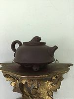 Side view of the dark brown Yixing pottery teapot showing fish feet supporting the base and round handle.