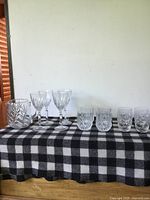 Wide view showing all crystal items on black and white checkered cloth, including decorative bowl on the left, two goblets in center, and five tumblers on right.