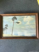 Overview of the full framed print showing coastal landscape scene with pine trees and ocean under a cloudy sky.
