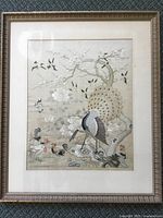 Full image of framed Chinese silk embroidery showing a peacock standing on a rock under blossoming tree branches with chickens and birds.