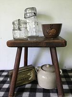 Two Atlas glass canisters and brown pottery bowl on rustic wooden stool