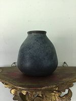 Front view of squat dark grey/black Grove pottery vase on shelf, showing rounded body and narrow opening.