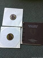 Two vinyl records in white paper sleeves alongside the original brown fold-out cover with visible damage.