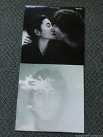 Two John Lennon LP albums stacked, front covers visible: one with John Lennon and Yoko Ono kissing, the other a faded portrait of John Lennon.