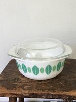 Front view of white glass Pyrex canister with green leaf and dot pattern and clear glass lid