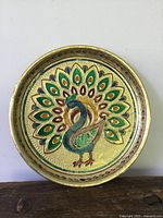 Front view of round metal enamel tray with peacock design and textured background