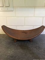 Front view of the curved wooden dish with four feet on a countertop.