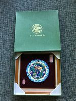 Green presentation box with gold dragon and Chinese characters on lid, open to reveal framed ceramic plate inside with protective corner supports.