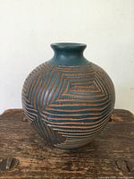 Angled front view of rounded blue and brown pottery vase showing the carved maze-like linear geometric pattern.