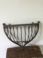 Front view of rustic wrought iron flower wall hanger showing curved basket shape with vertical bars and decorative scroll accents.