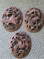 Three wooden oval plaques displayed on carpet background, showing detailed carvings of mythical creatures and traditional Chinese motifs.