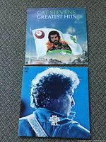 Top-down photo of two vintage LP record covers placed on carpet, Cat Stevens Greatest Hits on top, Bob Dylan's Greatest Hits Vol. II below.