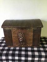 Front view of the vintage copper studded wood chest showing embossed sailing ship design.