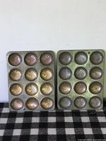 Two vintage metal baking sheets each with 12 shell-shaped molds for Madeline pastries.