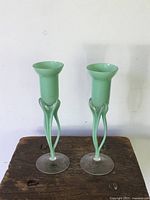 Pair of light green and clear glass stem vases on wooden surface with factory sticker visible on base of one vase.