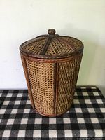 Side view of the round rattan and wood hamper showcasing its woven pattern and wooden frame.