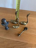 Set of three brass swans, metal bust figurine, and decorative metal key shown together on wooden surface with measuring tape for scale.