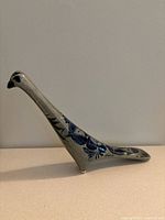 Side view of the gray ceramic long neck bird figurine showing hand-painted black and white floral motifs and the long slender neck.