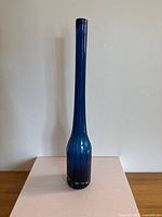Full profile view of tall cobalt blue blown glass vase on a flat surface with neutral background.