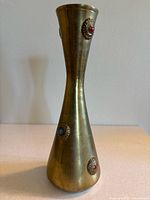 Full view of tapered brass vase showing red and turquoise inlays on embossed designs