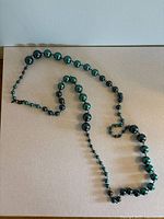 Full view of the necklace showing various sized teal glass beads laid out flat.