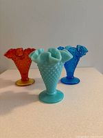 Set of three Fenton hobnail glass vases showing blue milk glass, translucent blue, and amberina colors with ruffled tops