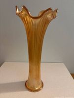 Front view of tall iridescent gold/amber carnival glass vase with ruffled top and vertical ribbing