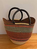 Front view of large multicolor straw basket with black leather wrapped handles showing detailed woven pattern and basket shape.
