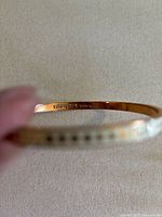 Close-up of interior of white enamel bangle bracelet showing gold-tone metal and marked Kate Spade & et cetera