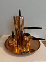 Photo showing full tea and coffee copper set on tray, featuring coffee pot, creamer, sugar bowl, all with black handles and finials, on round copper tray with label.