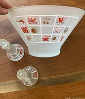 Photo showing the underside and side view of the frosted glass salad bowl and the two cruets, highlighting the mid-century grid pattern with various symbols in red, tan, and white.