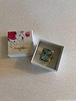 Top-down view of the ring inside a white Magnolia Jewelry box with floral design on the lid.