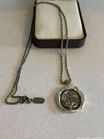 Front view of the silver pendant necklace with detailed Tree of Life design and chain with Pyrrha tag, resting on jewelry case.