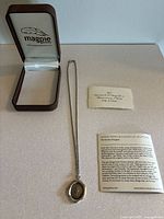 Full view of the pendant necklace laid out next to the opened jewelry box and informational cards on a flat surface.