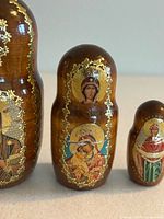 Close-up of mid-sized nesting doll depicting Virgin Mary with infant Jesus and another saint figure, showing hand-painted gold accents.