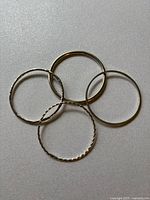 Four silver bangle bracelets laid flat overlapping, showing different textures and sizes.