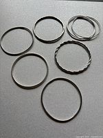 Photo of all six sterling silver bangle bracelets laid flat on a surface, showing various designs such as hammered, twisted, and plain styles.