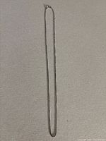 Full view of the 18 inch sterling silver box chain necklace with oval links lying flat on a surface.