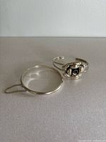 Both bracelets side by side on a flat surface, showing the bangle with chain and the floral cuff.