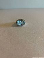 Front view of oval domed light blue faceted stone set in sterling silver ring on plain background.