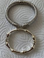 Two sterling silver cuff bracelets, one twisted cable design medium size and one bamboo design small size, shown together on white textured surface.