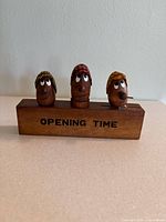 Front view of the teak wood base stand displaying the whimsical face heads with different hats serving as functional bar tools.