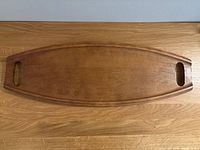 Top view of the wooden surfboard-shaped serving tray showing its full length, brown finish, and integrated handles.