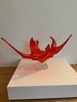 Front view of red glass art bowl with clear base, showing curved wing-like design