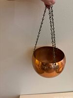 Copper hanging plant pot being held to show shape, finish, and chain length.