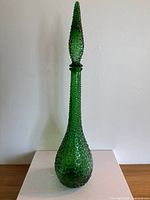 Full view of tall green glass genie bottle with hobnail texture and pointed stopper.