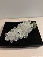 Side angle view showing the frosted glass grapes and green leaf sitting on a black display base.