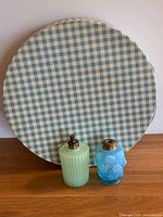 Photo showing two vintage perfume bottles in front of a closed round hat box covered with blue and white gingham paper.